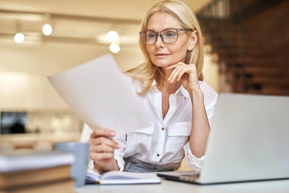 Woman reading a document and sitting at a laptop
